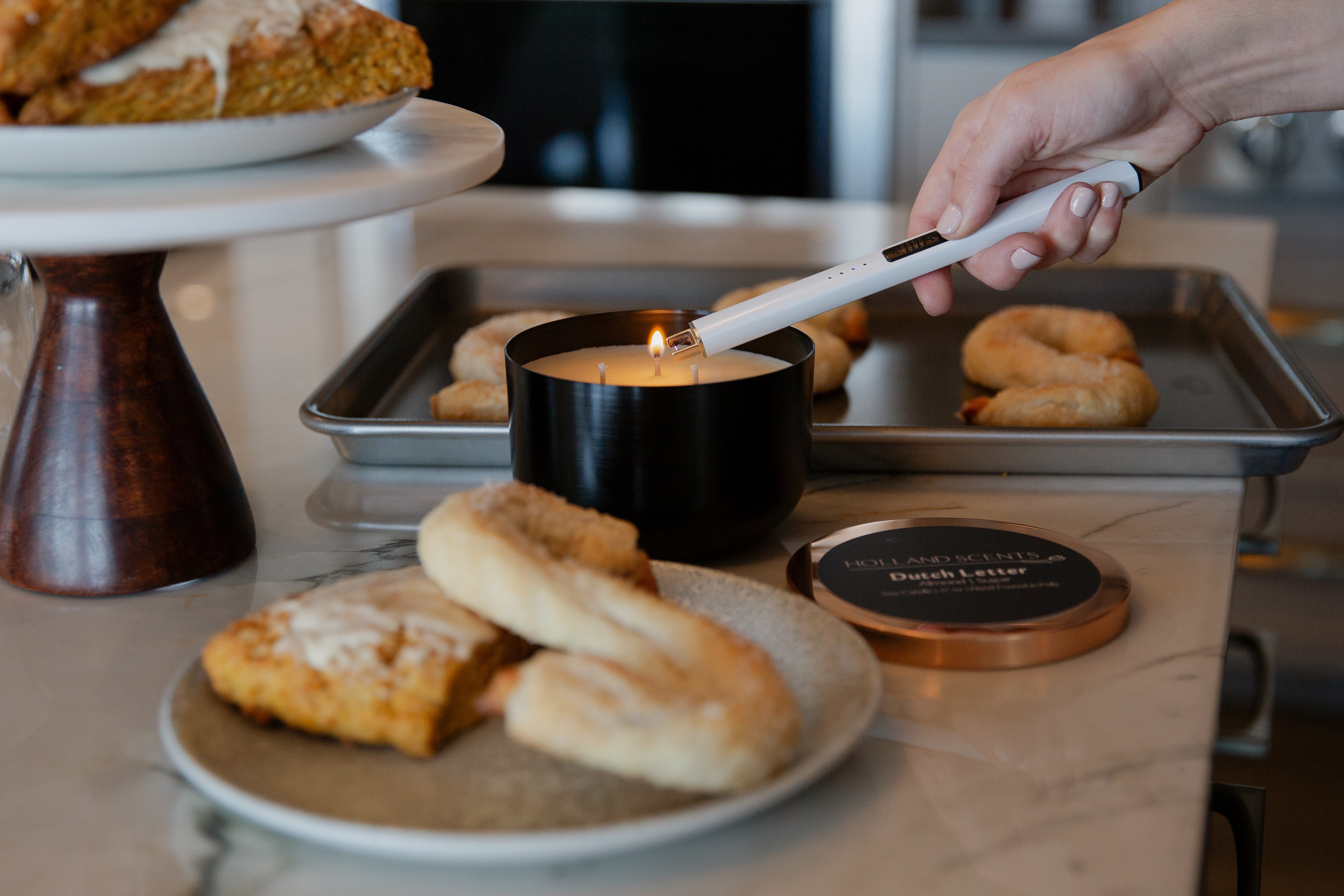 Holland Scents Dutch Letter soy candle being lit beside fresh baked pastries, Pella, Iowa