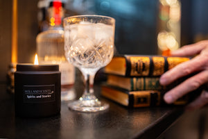 Holland Scents Spirits and Stories soy candle lit beside a gin cocktail and stacked books, Pella, Iowa